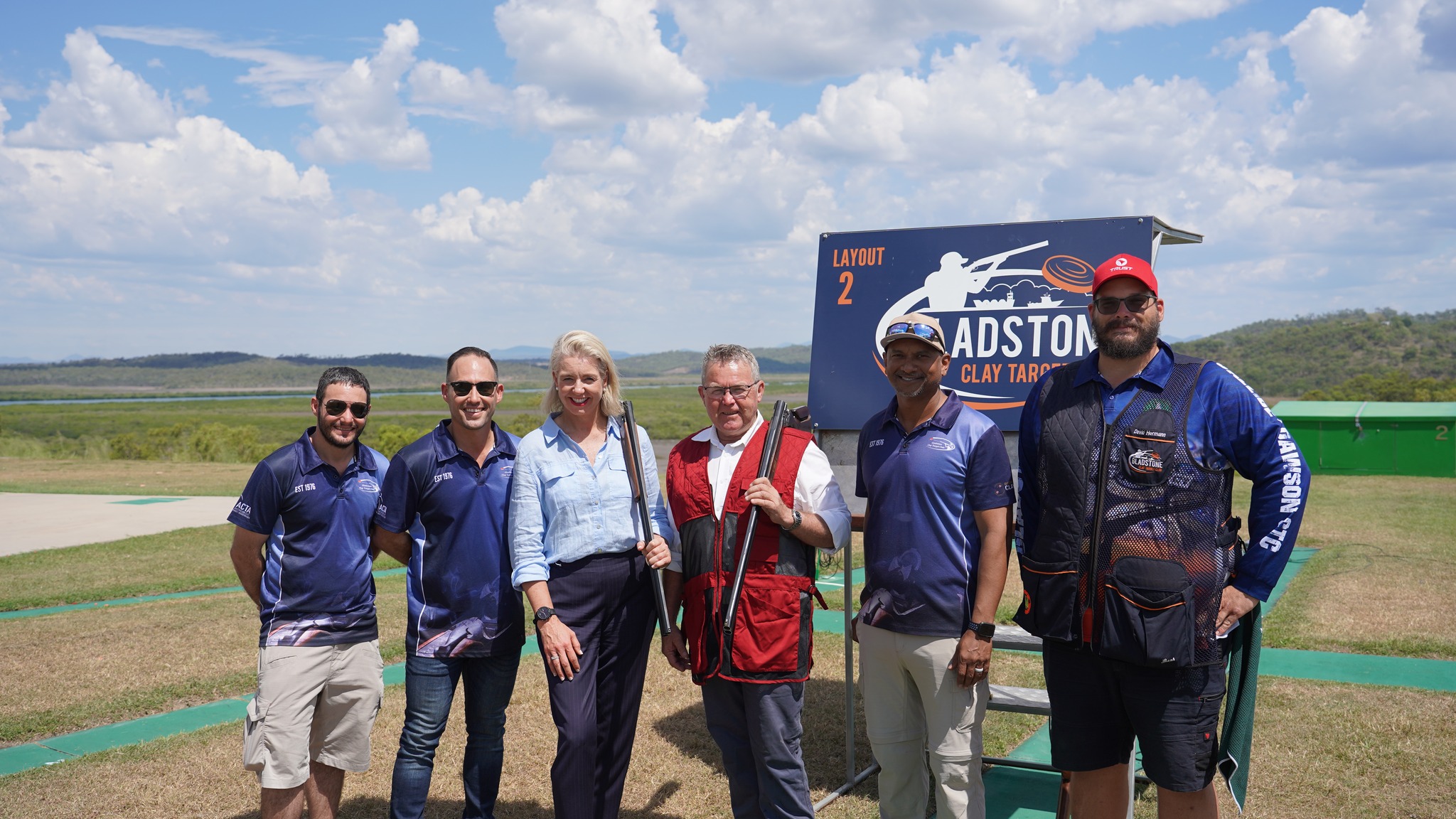 Golden wheat field stretching toward distant tree line under bright blue sky with scattered white clouds and dirt road in foreground.